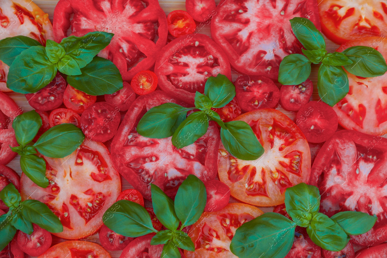 Photo of Cut tomatoes of different sorts with basil on wooden table, flat lay