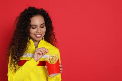 African American woman with French fries on red background, space for text