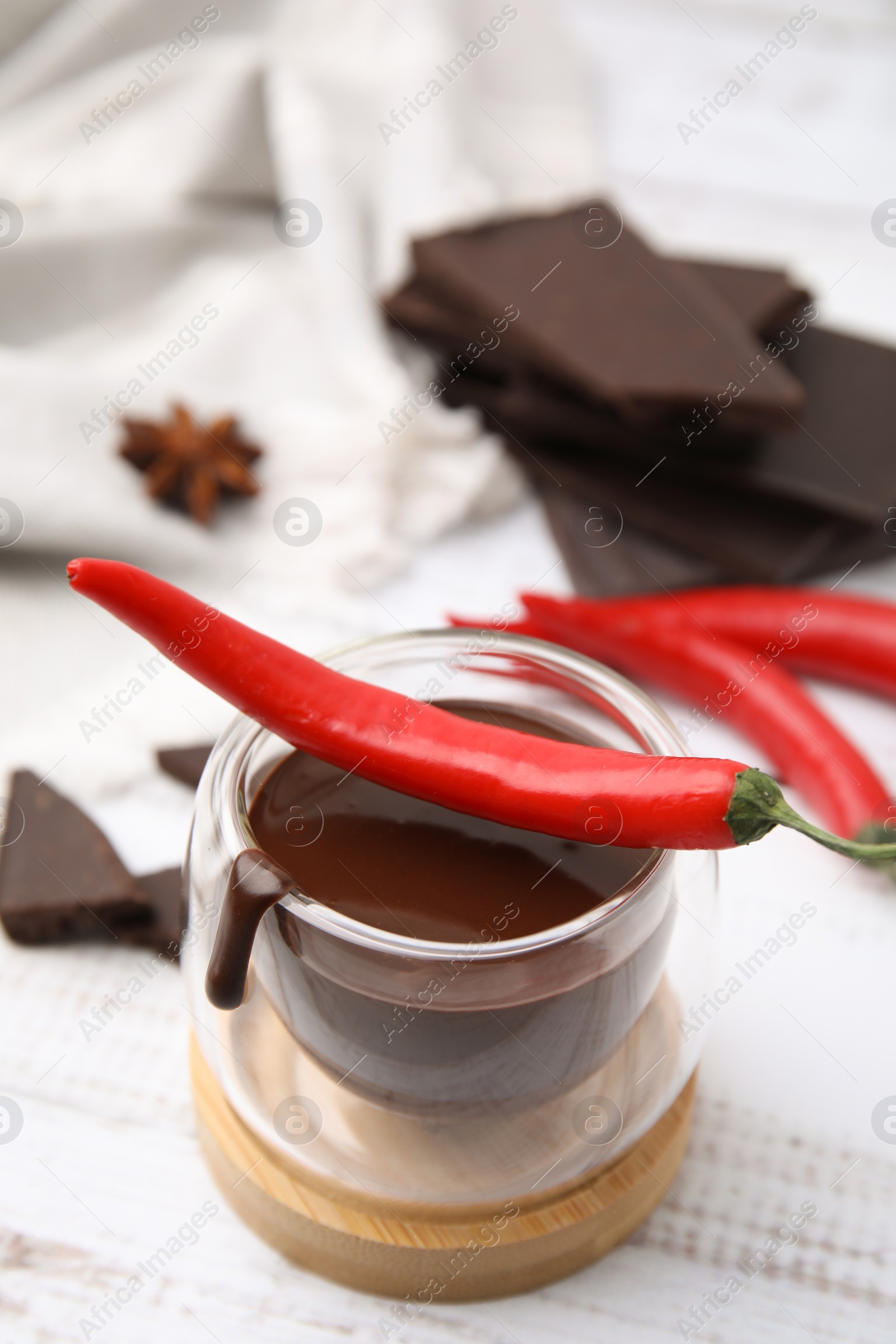 Photo of Glass of hot chocolate with chili pepper on white wooden table, closeup