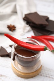 Glass of hot chocolate with chili pepper on white wooden table, closeup