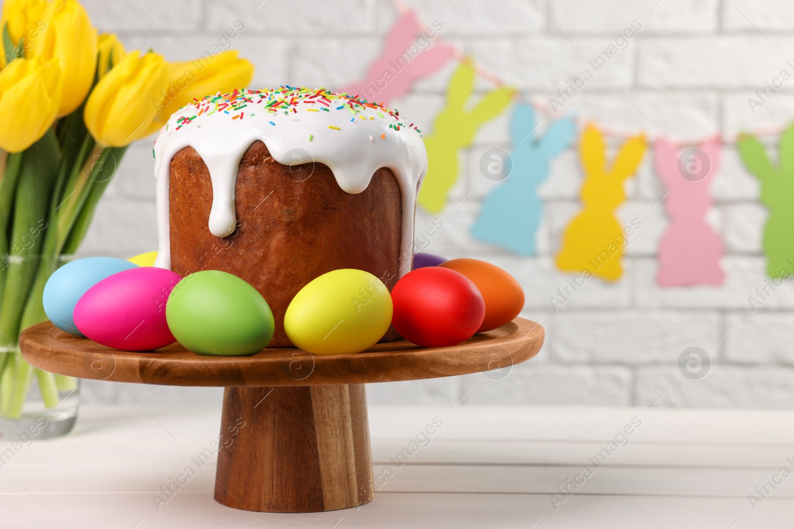 Photo of Stand with tasty Easter cake and decorated eggs on white wooden table. Space for text