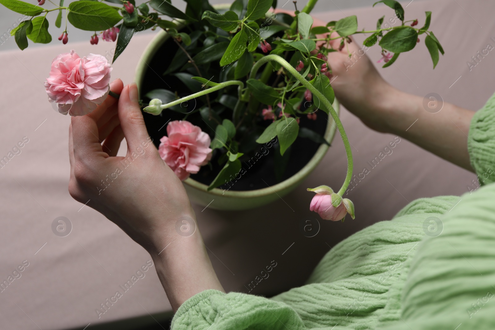 Photo of Beautiful ikebana for stylish house decor. Woman create floral composition with fresh ranunculus and carnation flowers at beige table, top view