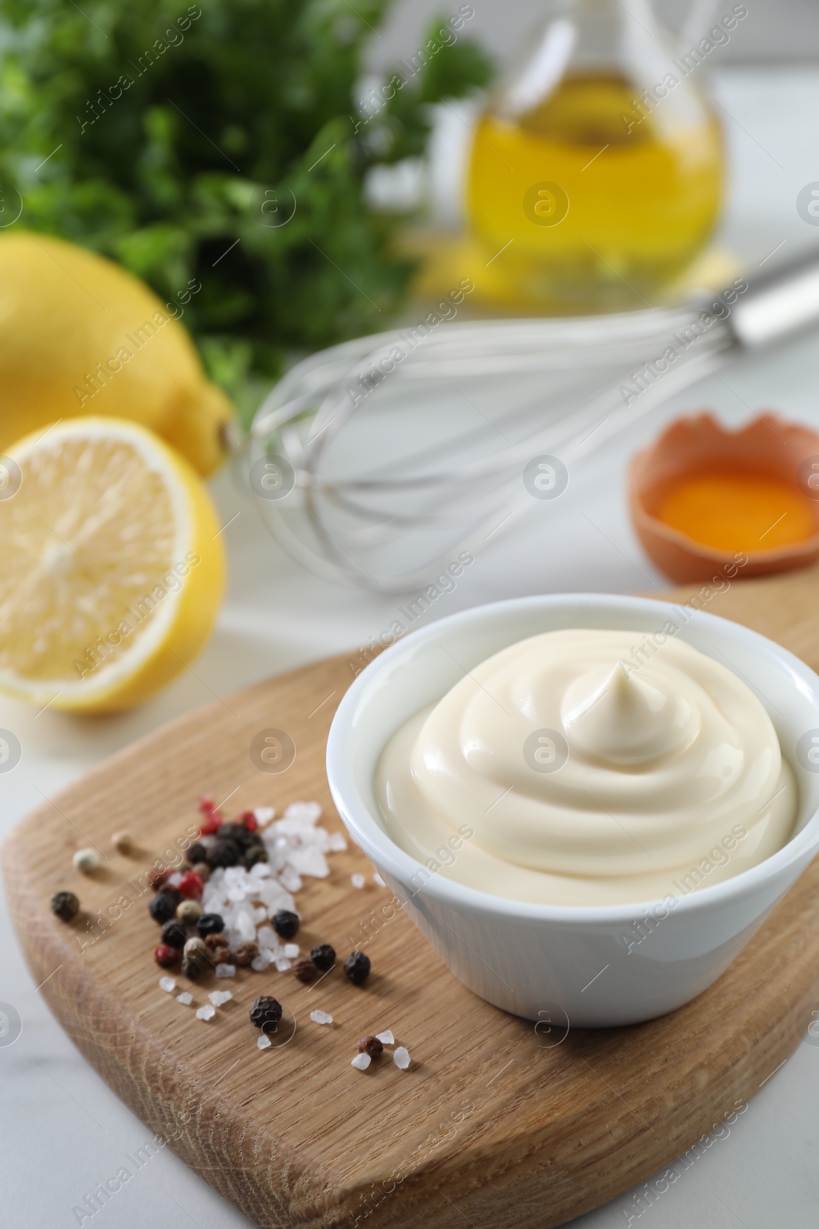 Photo of Tasty mayonnaise sauce in bowl, ingredients and spices on white table, closeup