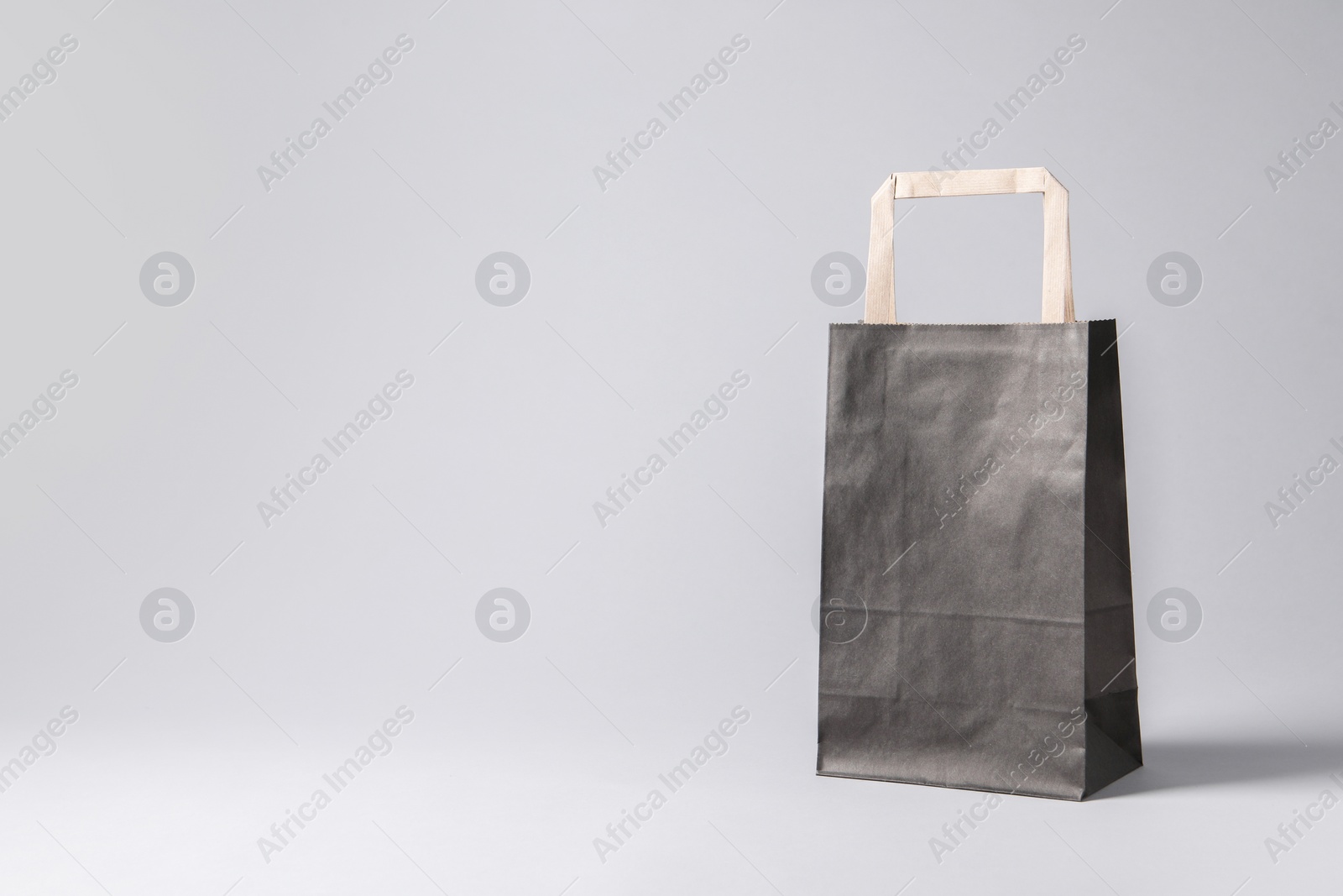 Photo of Black paper bag on light grey background, space for text