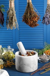 Mortar with pestle and many different herbs on blue wooden table, closeup