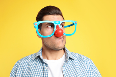 Photo of Emotional man with funny glasses on yellow background. April fool's day