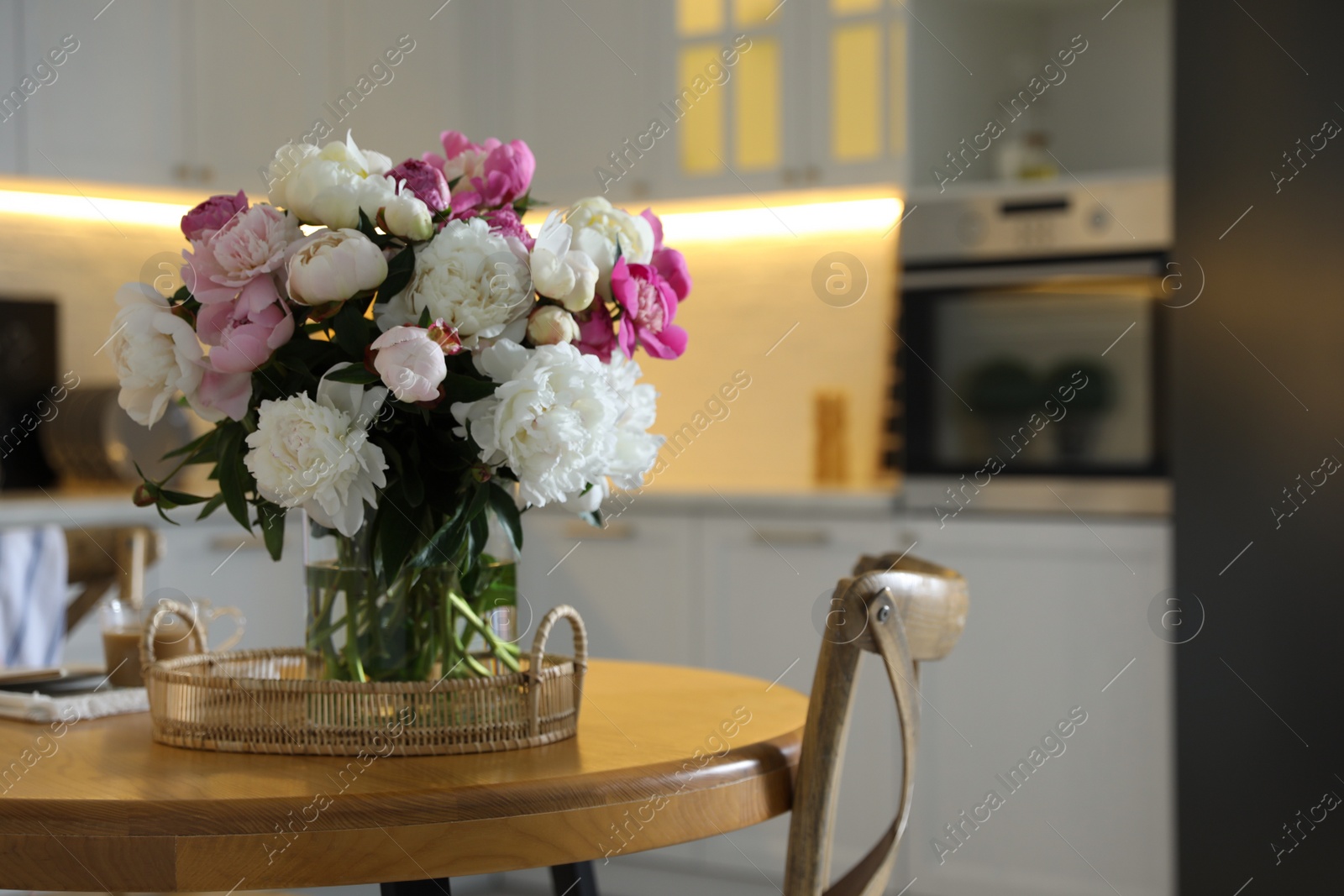 Photo of Beautiful peonies in vase on wooden table in kitchen. Space for text