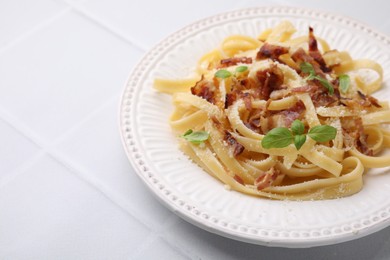 Photo of Tasty pasta with bacon and basil on white tiled table, space for text