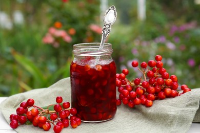 Jar of tasty jam and viburnum berries on table outdoors