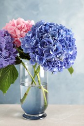 Photo of Vase with beautiful hortensia flowers on light table against color background