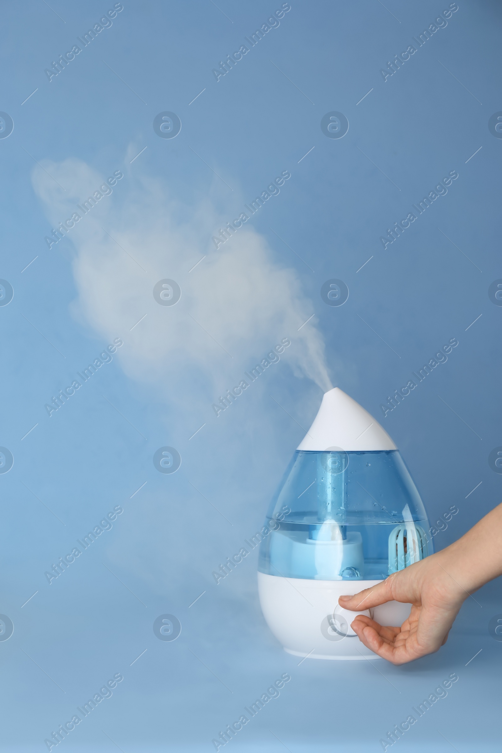 Photo of Woman using modern air humidifier on light blue background, closeup