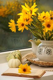 Photo of Composition with beautiful flowers, pumpkins and book on windowsill. Autumn atmosphere