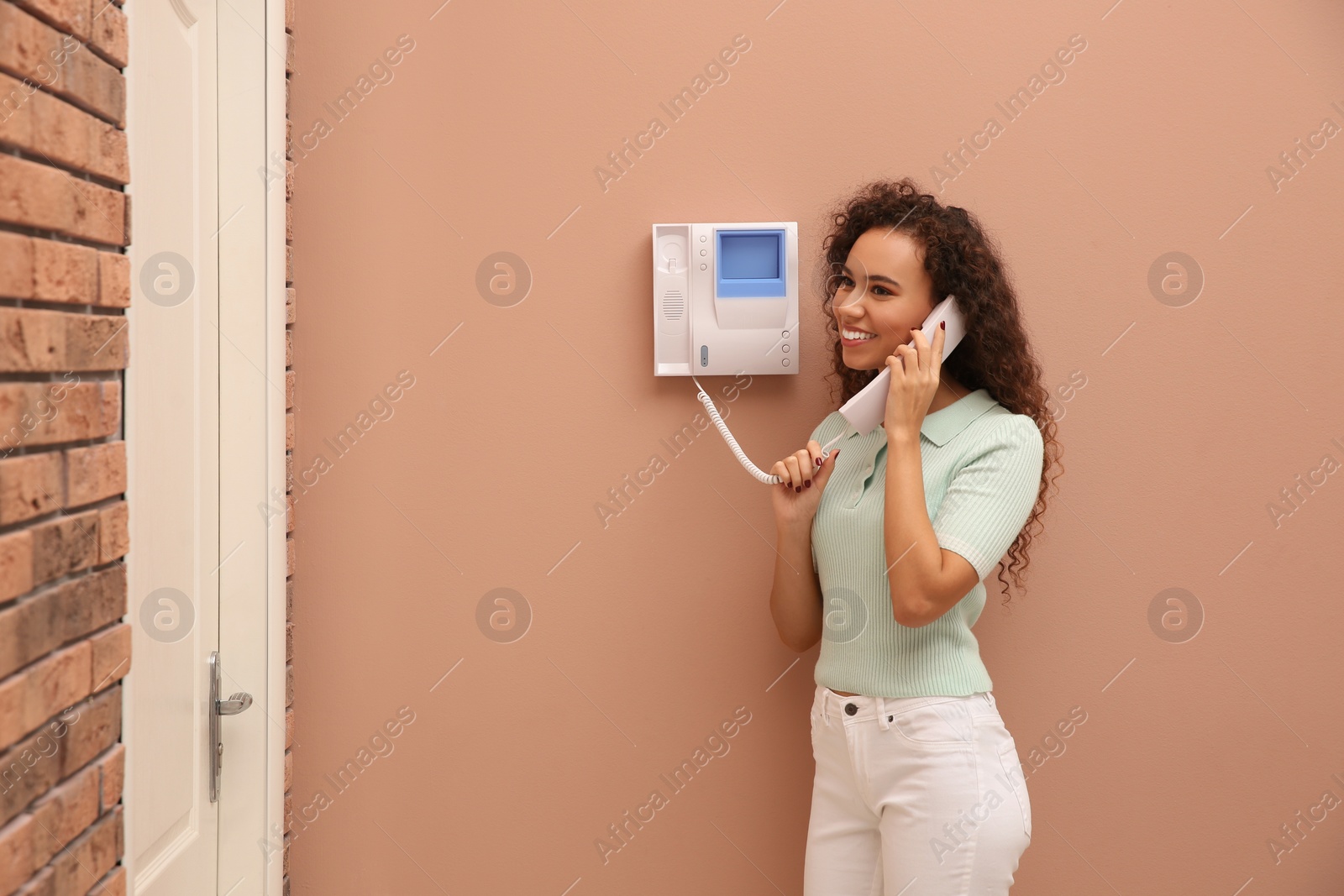 Photo of Young African-American woman answering intercom call indoors