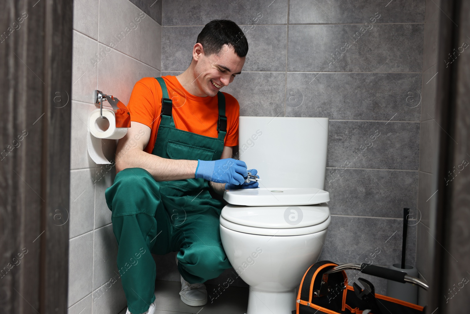 Photo of Smiling plumber repairing toilet bowl in water closet