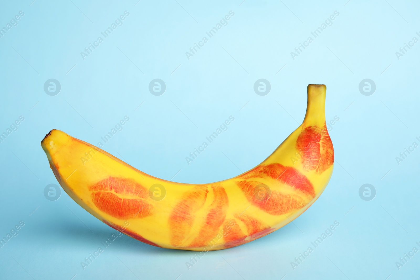 Photo of Fresh banana with red lipstick marks on blue background. Oral sex concept