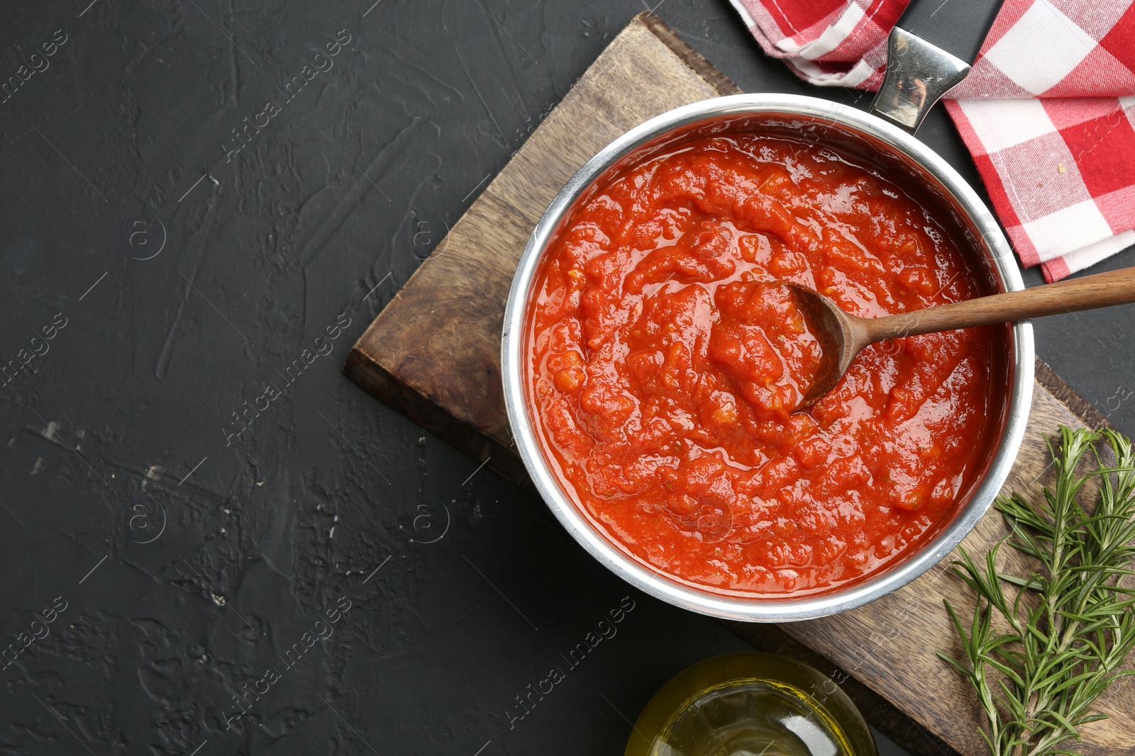 Photo of Homemade tomato sauce in pot, spoon and fresh ingredients on dark textured table, flat lay. Space for text