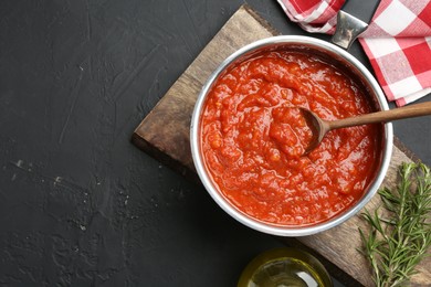 Homemade tomato sauce in pot, spoon and fresh ingredients on dark textured table, flat lay. Space for text