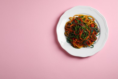 Photo of Plate of spaghetti painted with different food colorings on pink background, top view. Space for text