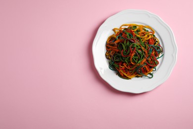 Plate of spaghetti painted with different food colorings on pink background, top view. Space for text