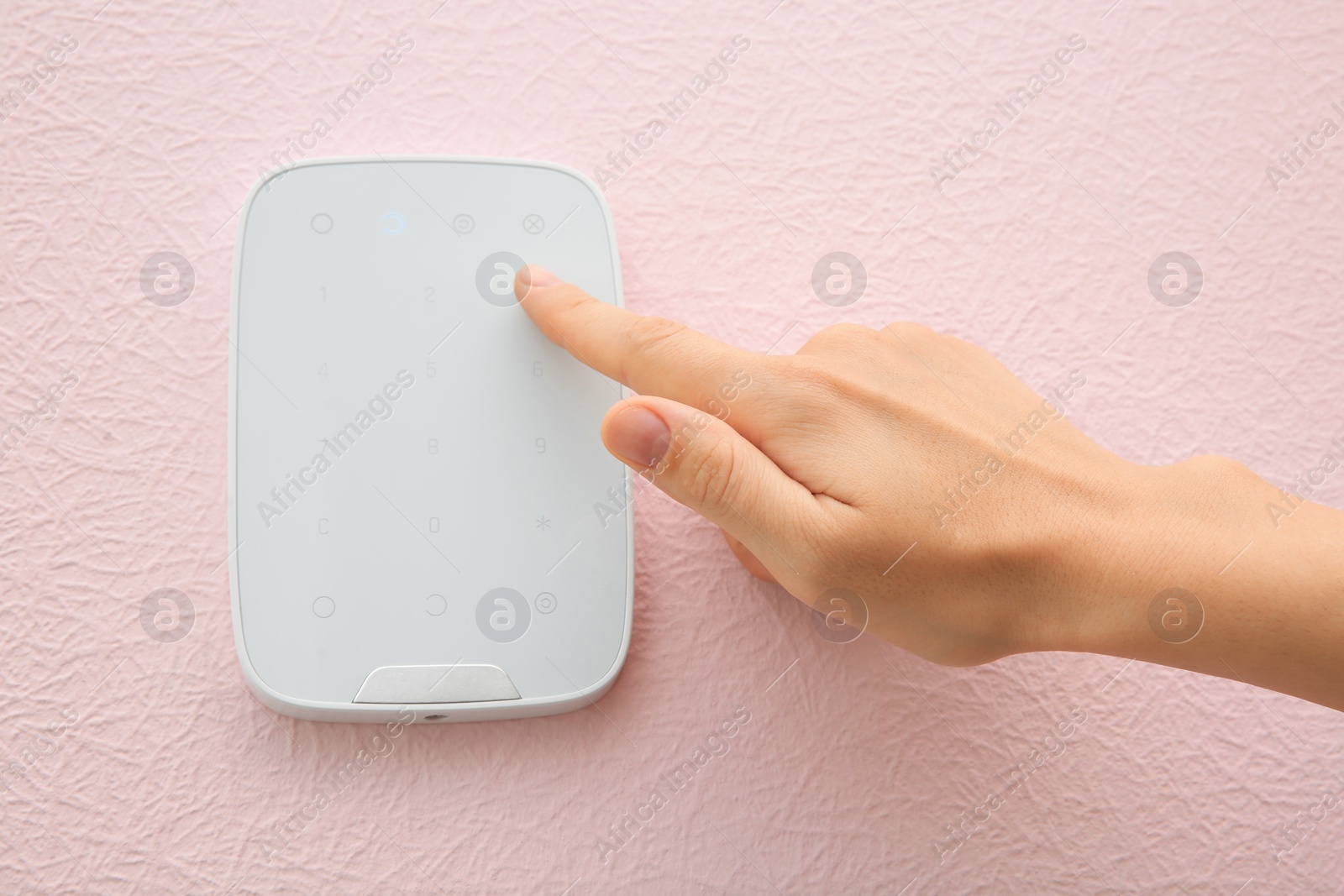 Photo of Young woman entering code on alarm system keypad indoors