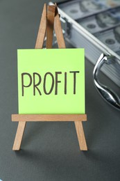 Photo of Economic profit. Easel with note and banknotes in briefcase on grey table, closeup