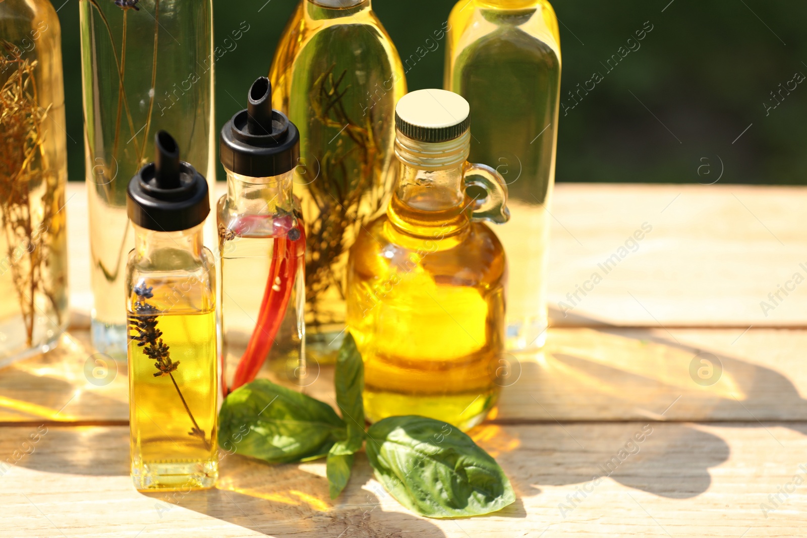 Photo of Many different cooking oils on wooden table against blurred green background, closeup. Space for text