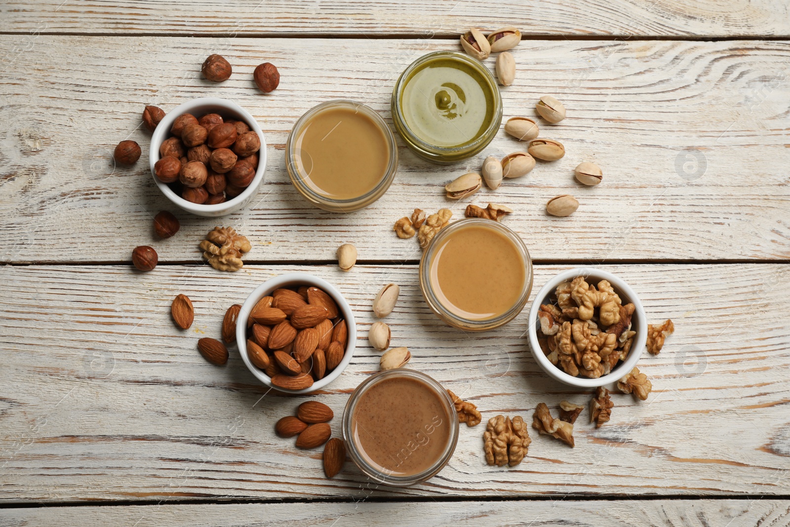 Photo of Jars with butters made of different nuts and ingredients on white wooden table, flat lay