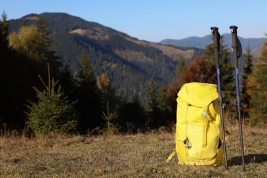Pair of trekking poles and backpack in mountains on sunny day, space for text