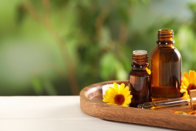 Photo of Bottles of essential oils and beautiful calendula flowers on white wooden table outdoors, space for text