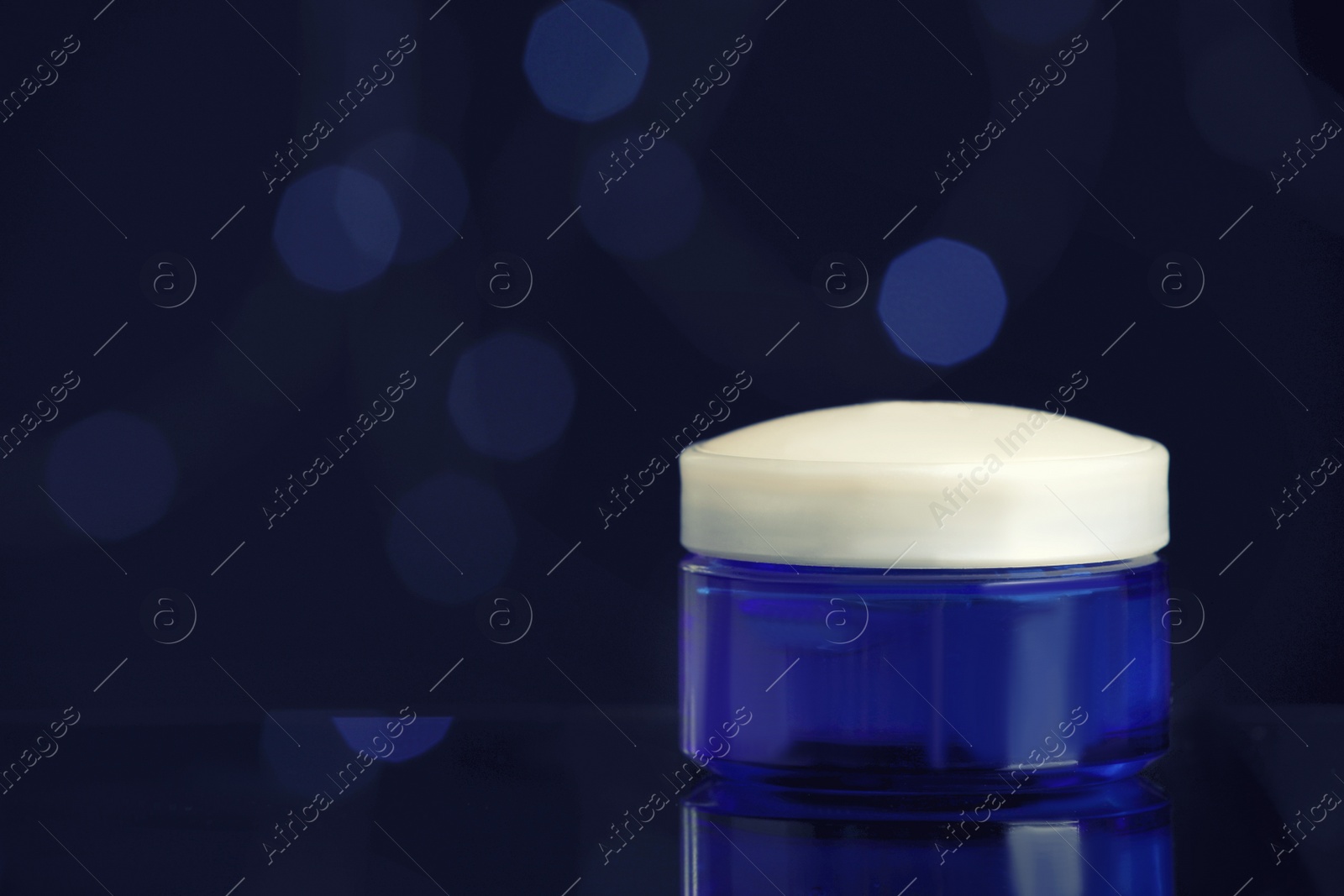 Photo of Jar of cream on table against blurred lights, space for text