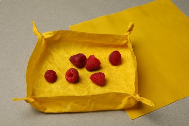 Photo of Orange reusable beeswax food wraps with fresh raspberries on grey background