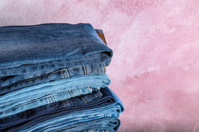 Photo of Stack of different jeans on pink background, closeup