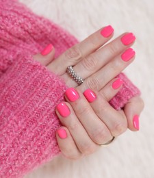 Photo of Woman showing her manicured hands with pink nail polish on faux fur mat, closeup