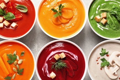 Various cream soups in bowls on grey background, top view