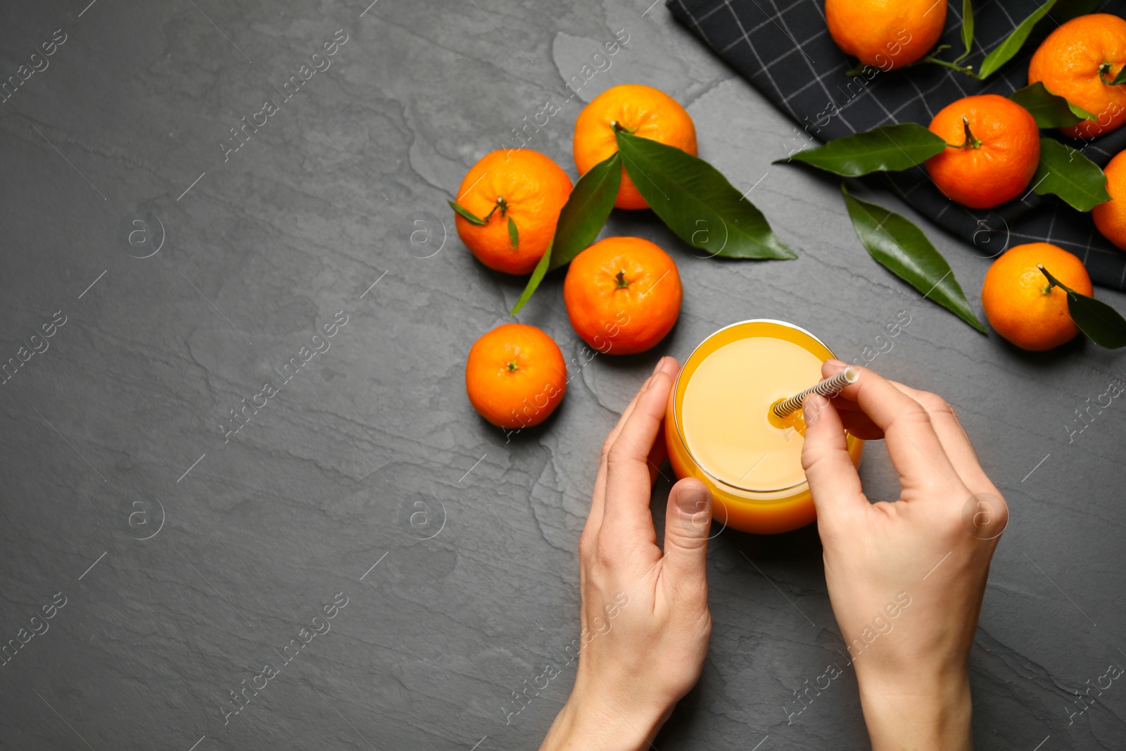 Photo of Woman with glass of fresh tangerine juice at black table, top view. Space for text