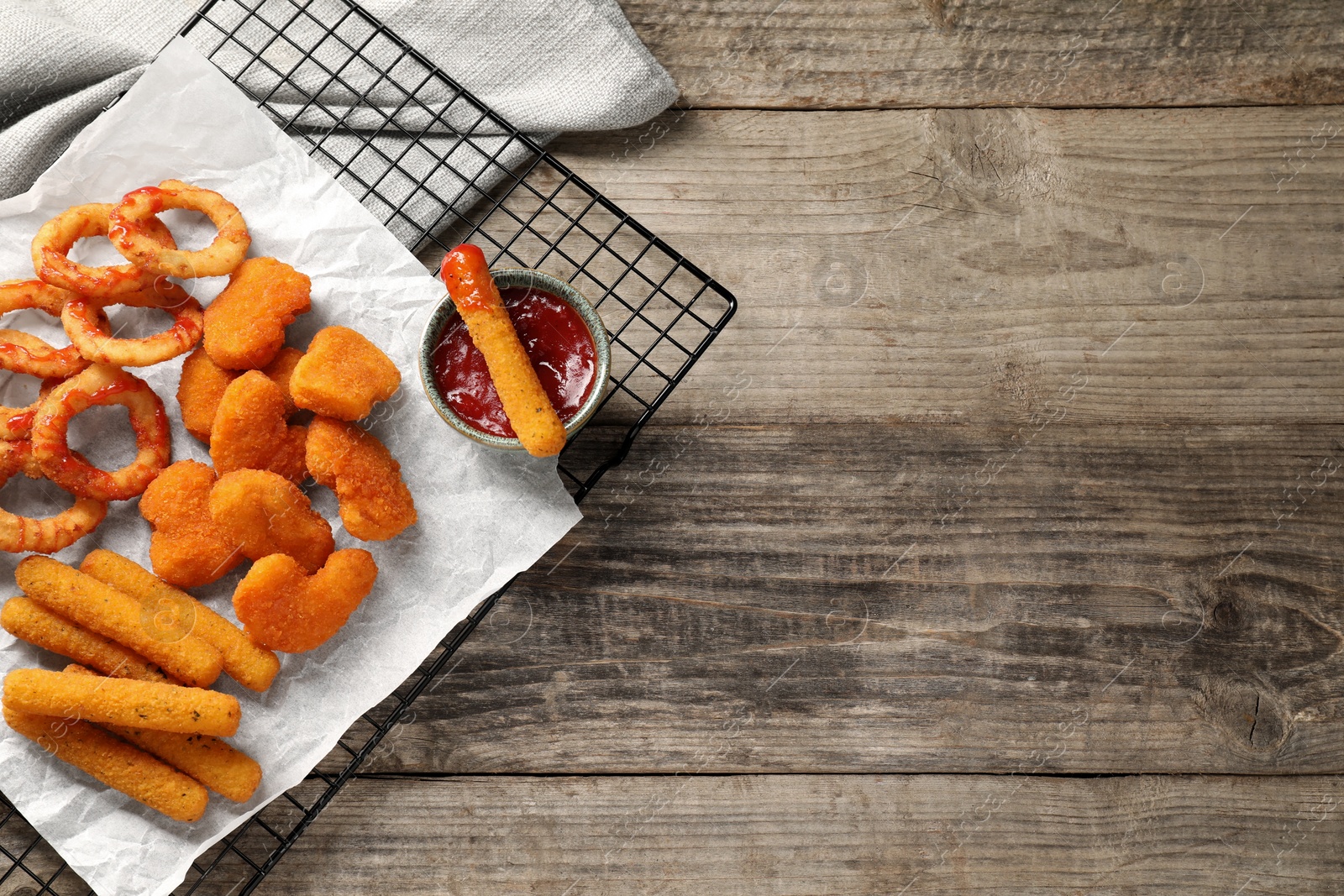 Photo of Tasty chicken nuggets, fried onion rings, cheese sticks and ketchup on wooden table, top view. Space for text