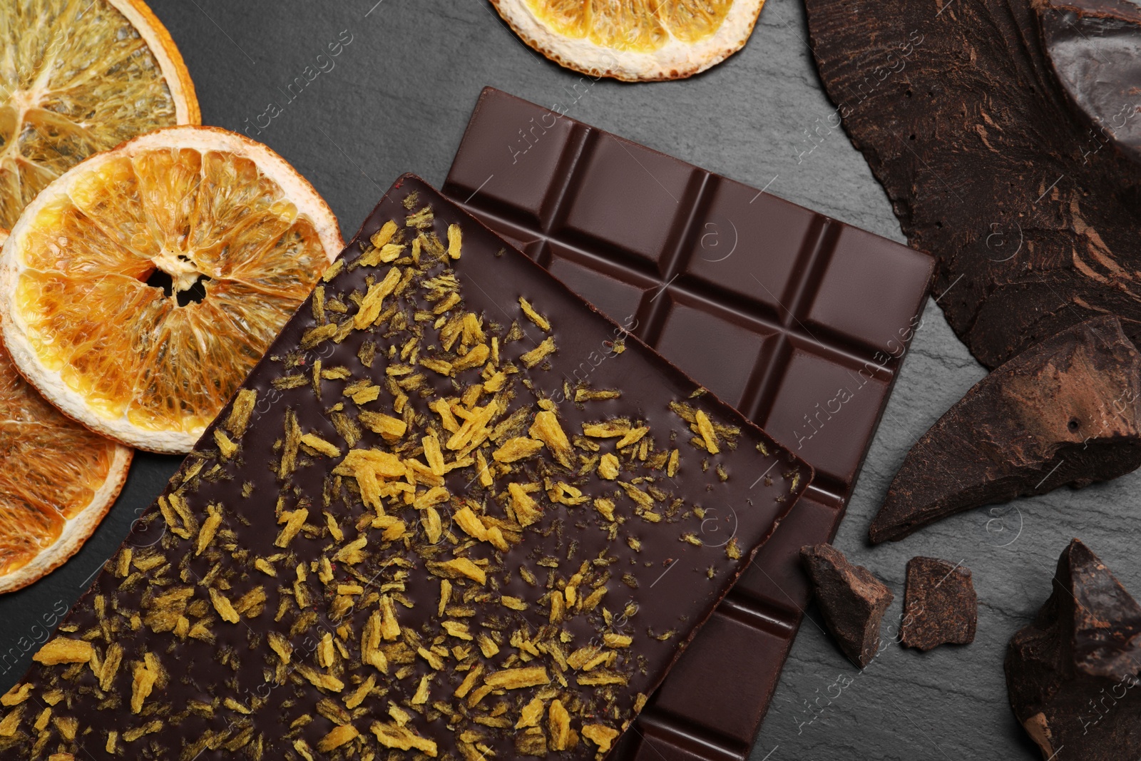 Photo of Chocolate bars with freeze dried orange on slate table, flat lay