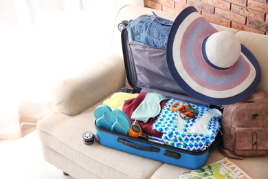 Photo of Open suitcase with different clothes and accessories on sofa indoors. Packing for vacation