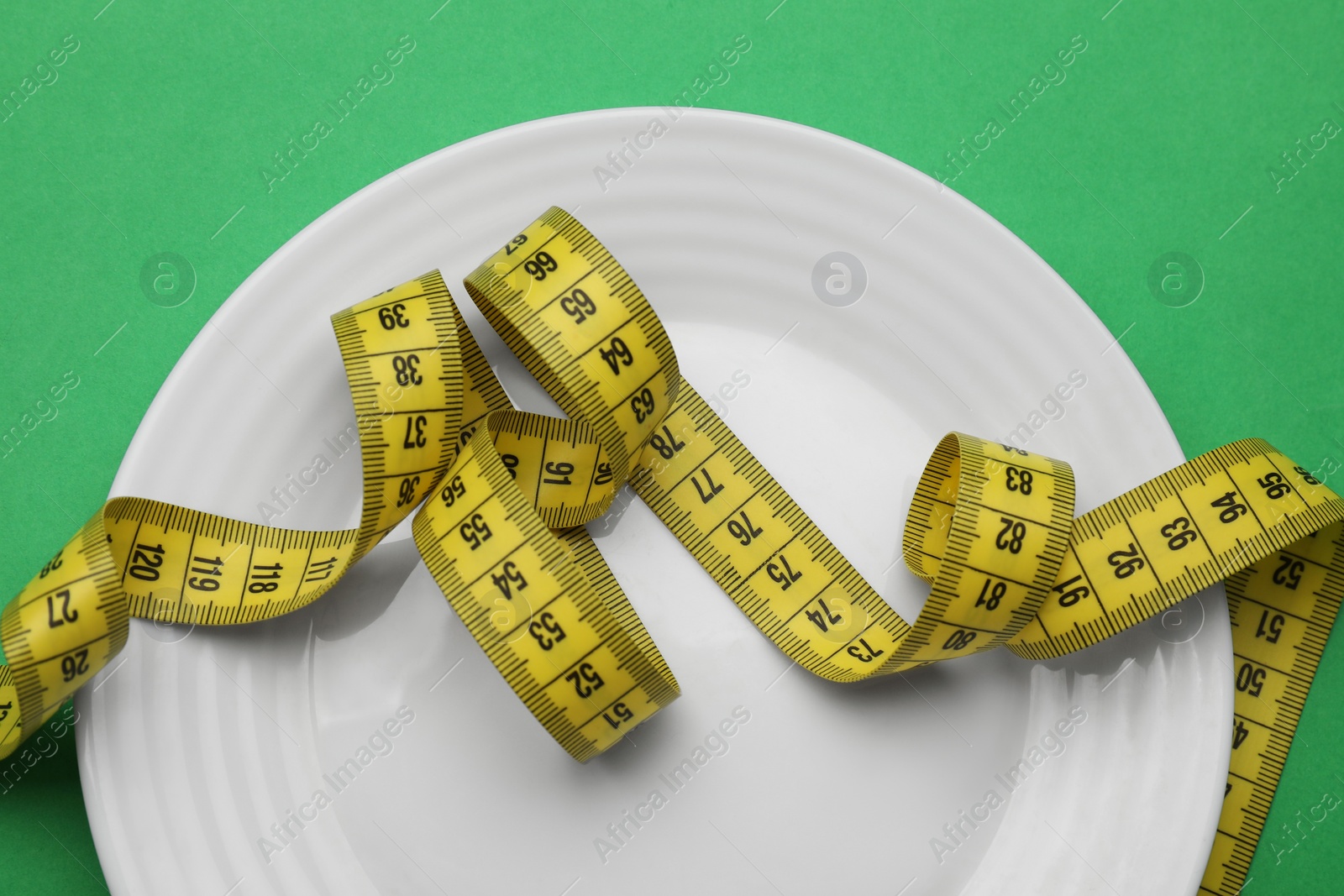 Photo of Plate and measuring tape on green background, top view. Diet concept