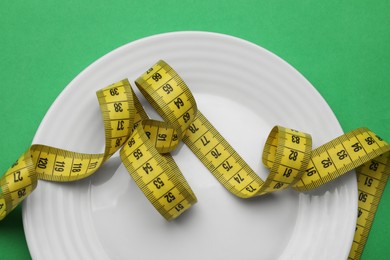 Plate and measuring tape on green background, top view. Diet concept