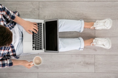 Photo of Young man with cup of coffee using laptop while sitting on floor, top view