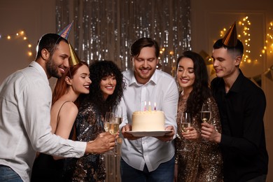 Happy friends with tasty cake and glasses of sparkling wine celebrating birthday indoors