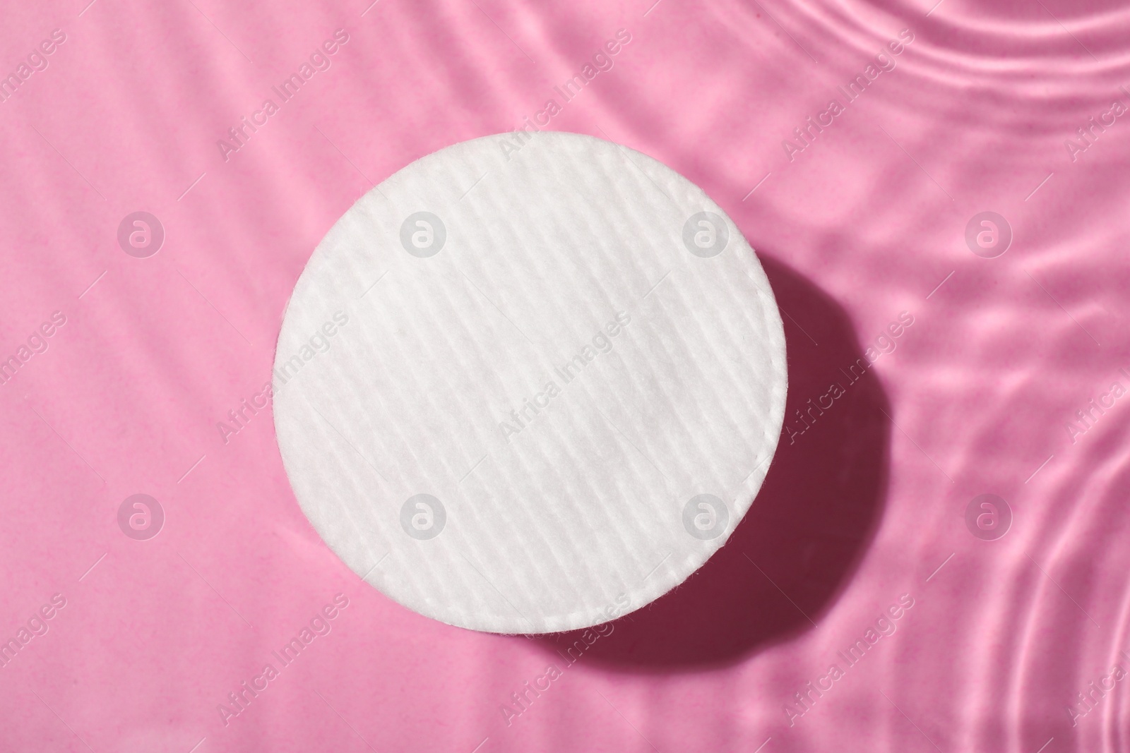 Photo of Cotton pad and micellar water on pink background, top view