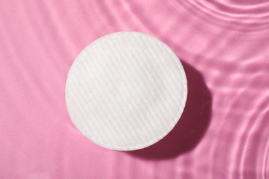 Photo of Cotton pad and micellar water on pink background, top view