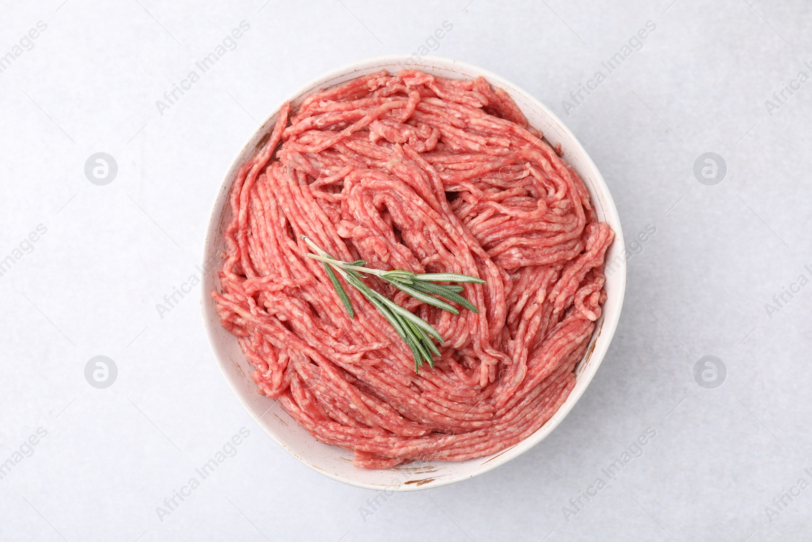 Photo of Fresh raw ground meat and rosemary in bowl on light table, top view