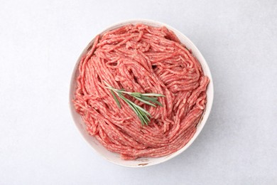 Photo of Fresh raw ground meat and rosemary in bowl on light table, top view