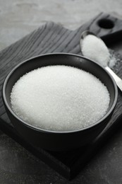 Photo of Granulated sugar in bowl on grey table, closeup