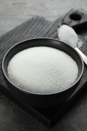 Granulated sugar in bowl on grey table, closeup