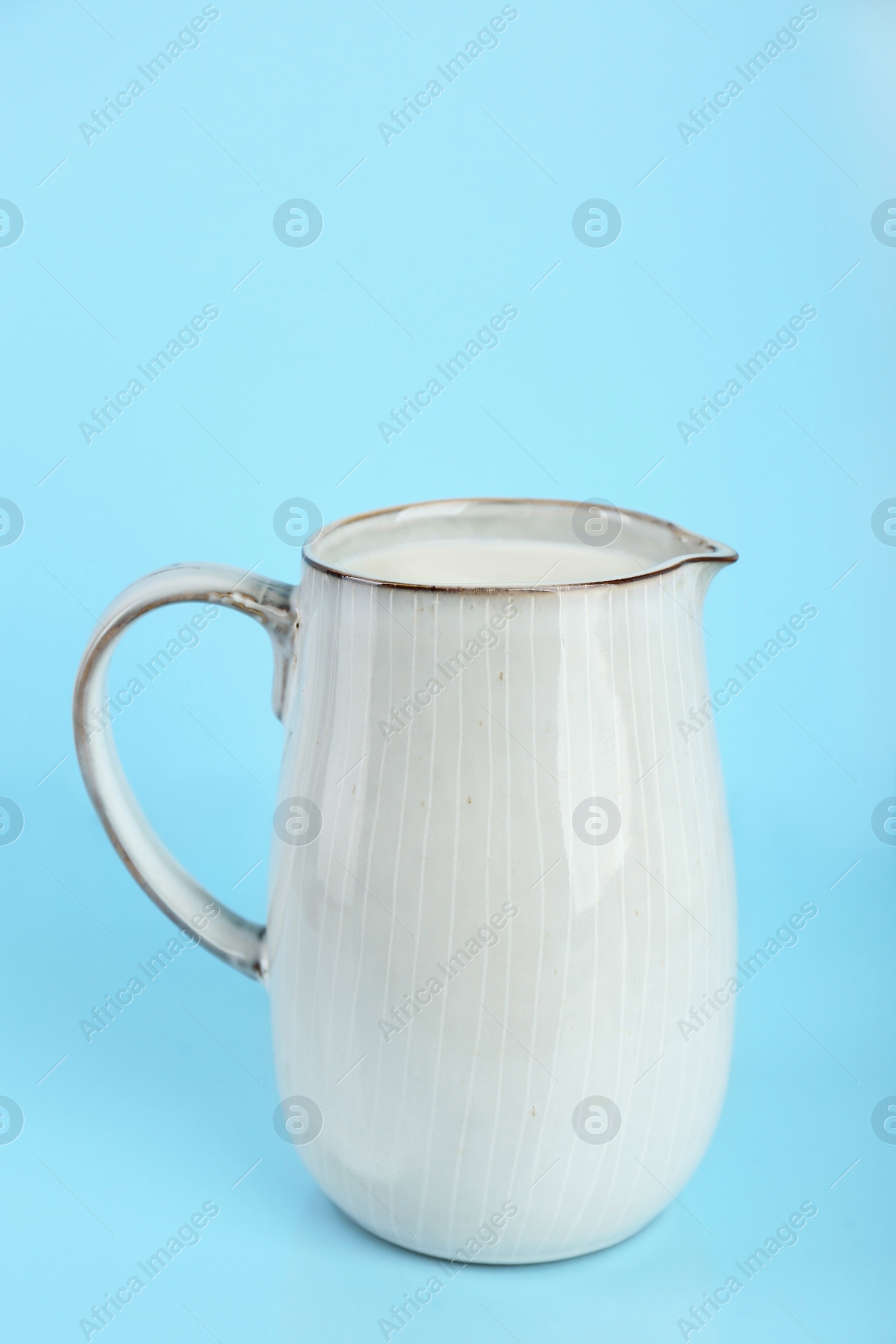 Photo of Jug of fresh milk on light blue background