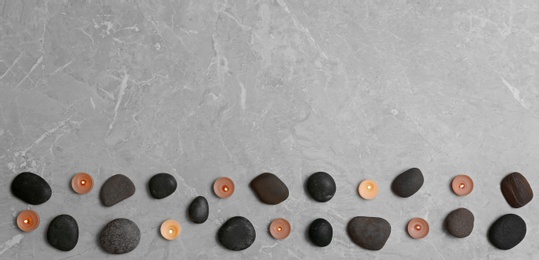 Flat lay composition with spa stones and lit candles on grey marble background, space for text